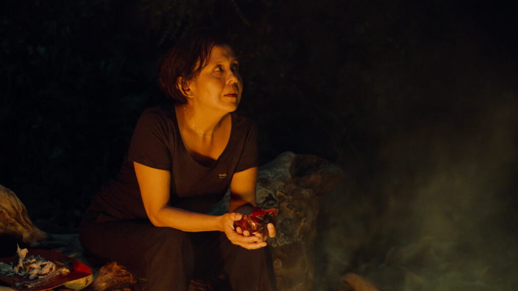 Abigail sitting on a rock on the island at night in Triangle of Sadness